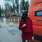 A reporter in red documents a crime scene with investigators in protective suits.