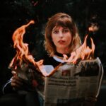 A young woman holding a burning newspaper, creating a dramatic scene.