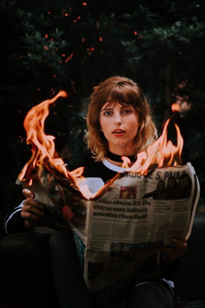 A young woman holding a burning newspaper, creating a dramatic scene.