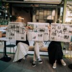 Three people hold newspapers with 'World Photography Day' outdoors.