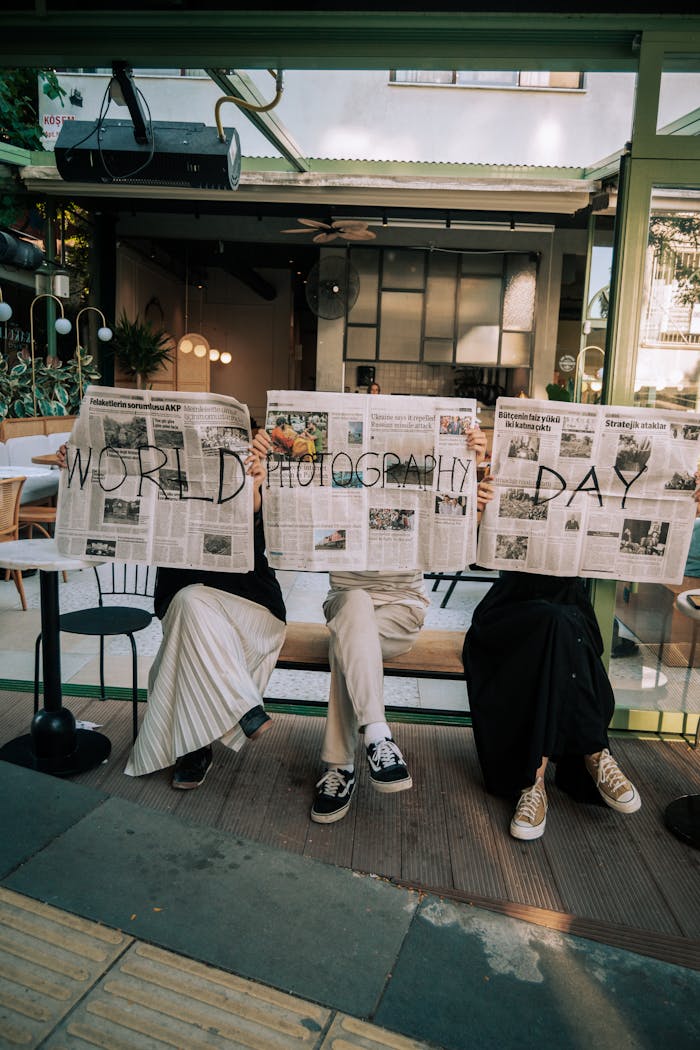Three people hold newspapers with 'World Photography Day' outdoors.