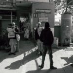 Black and white of serious men in casual clothes standing on street and reading notes in newspapers